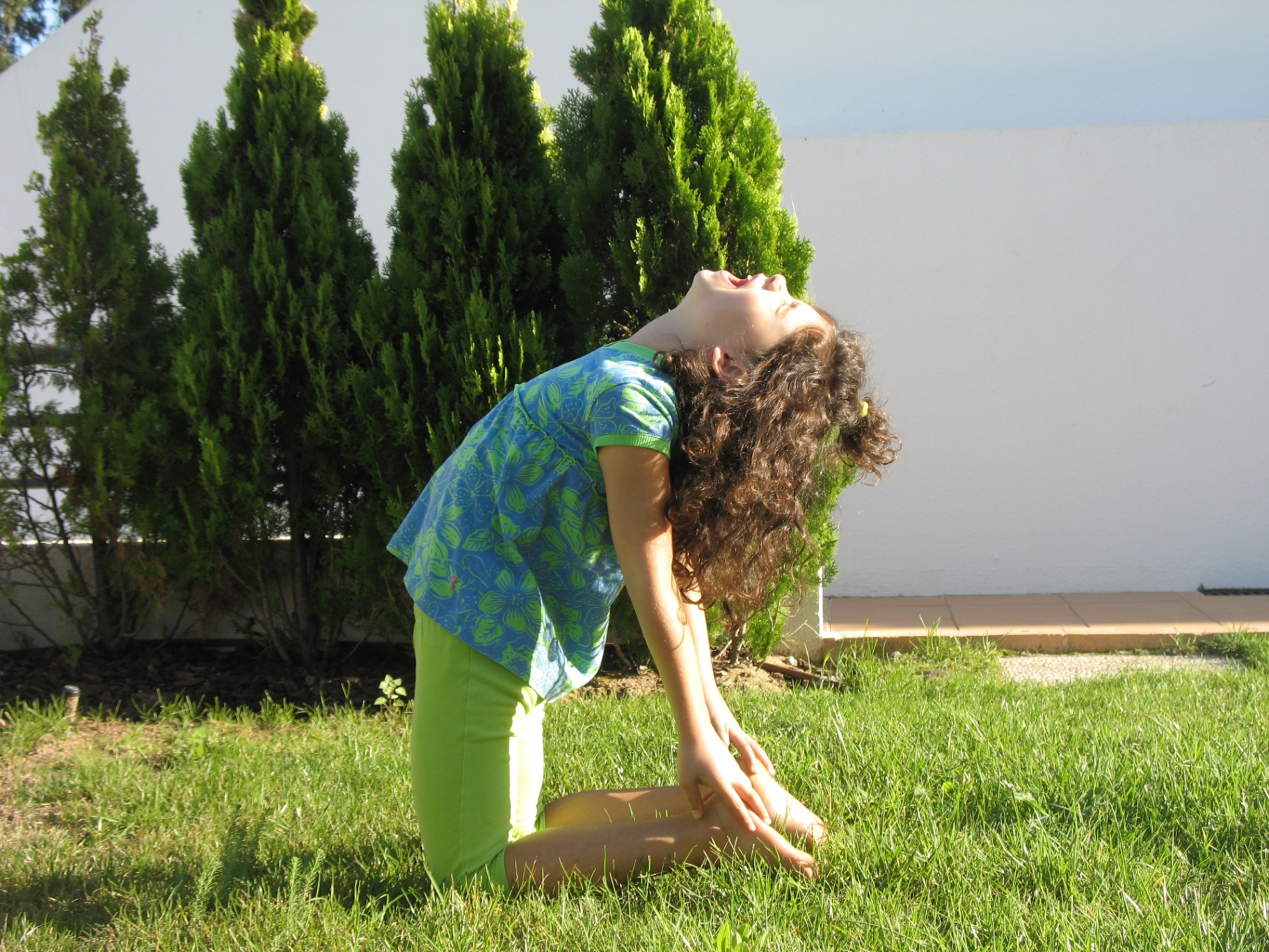 Criança em postura do camelo (Ustrasana) num jardim